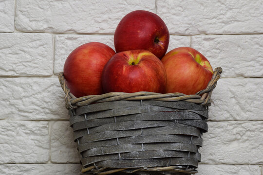 Basket with red apples on a background of a brick light wall. The basket is at the bottom center of the frame.