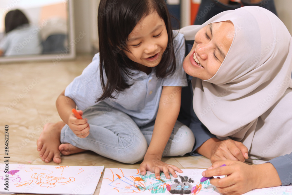 Wall mural Asian muslim mother drawing with her daughter, single mom teaching baby girl, learning on the floor, happy family