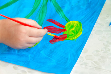 The child draws a bright picture. Large strokes of paint on paper.
