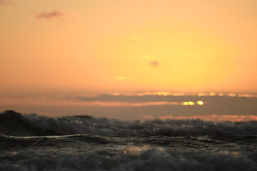 Waves crashing in orange sunset over the sea