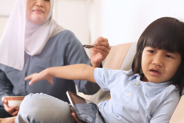 Asian muslim mother trying to feed her baby girl, little daughter refusing food that mother giving...