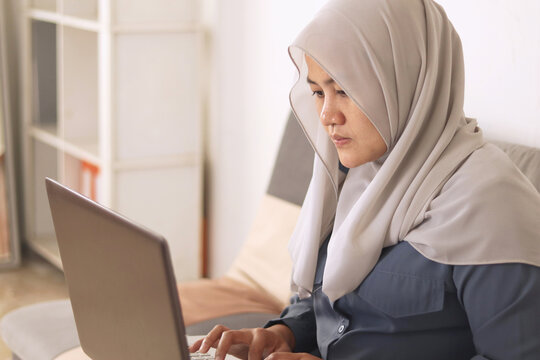 Asian Muslim Woman Wearing Hijab Smiling While Typing On Her Laptop, Work From Home Concept. Young Successful Female Entrepreneur Working At Home