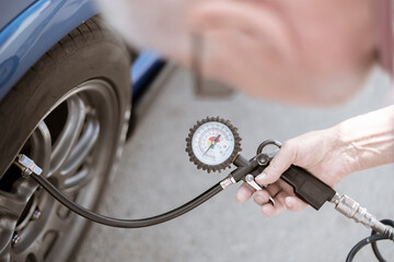 person pump up the car wheels tires with a compressor with manometer