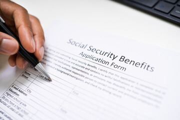 Person's Hand Filling Social Security Benefits Application Form