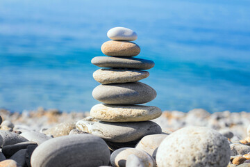 Fototapeta na wymiar Pyramid of sea pebbles on the beach against the sea on a Sunny day