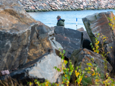 An alone man fishing at the pier behing large blocks of rocks.