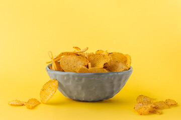 side view green plate with delicious corrugated golden potato chips fried and salted on a yellow...