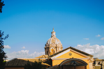 Fototapeta na wymiar Rome, Italy - An horizontal shot of the Basilica Aemilia partially covered by the roof of a yellow house during a clear sky afternoon.