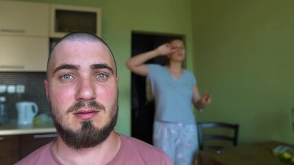 In the foreground is a Bald Man with an Imperturbable Facial Expression in the background a Dancing Woman. Family Relationships, Cuisine, Home Life, Quarantine.