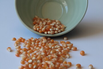 Corn seed in green ceramic bowl isolated on white background. Spilled seed pile.