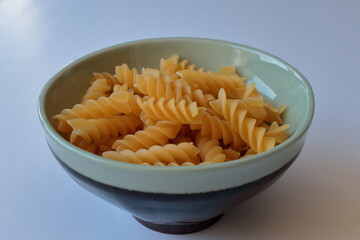 Uncooked raw Italian fusilli pasta in a ceramic bowl on white background. Side view.