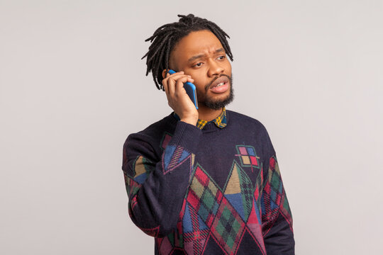 Concerned African Man With Dreadlocks Speaking Cell Phone, Discussing Problems, Free Calls, Connection. Indoor Studio Shot Isolated On Gray Background