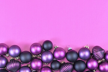 Seasonal dark purple and pink Christmas tree bauble ornaments at bottom of pink background with empty copy space