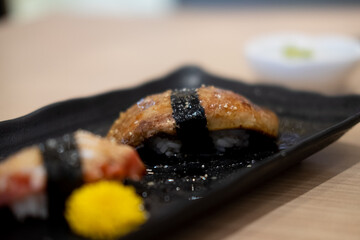 Grilled foie gras sushi on black plate.