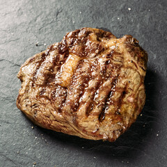 grilled piece of juicy meat with spices on a black stone background, ribeye