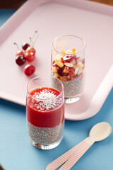 chia pudding with berry mousse in a glass glass on a light blue background with a pink tray in the background