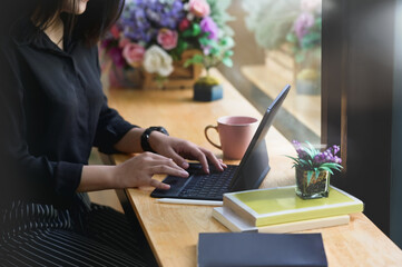 Cropped shot of young female freelancer typing on tablet in comfortable workspace.