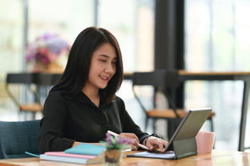 Portrait of businesswoman working on digital tablet with stylus pen while sitting on worktable in...