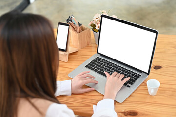 Overhead shot of female working with laptop and smartphone on wooden desk.