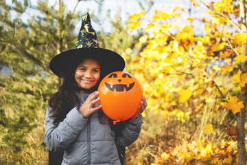 Halloween kids. Portrait smiling girl with brown hair in witch hat with pumpkin balloon.