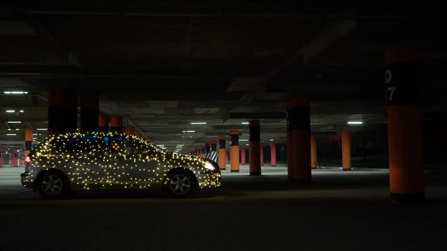 Car from purge at night in the parking lot. The hatchback is wrapped in a garland. The car is decorated for Halloween slowly parks in the mall.