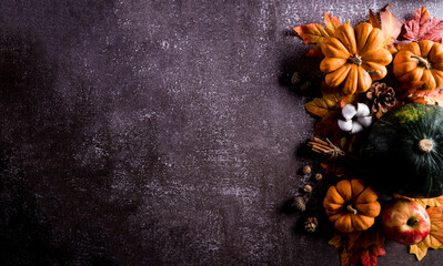 Obraz na płótnie Canvas Thanksgiving background decor from dry leaves and pumpkin on dark stone background. Flat lay, top view with copy space