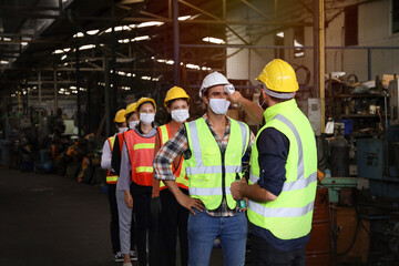 Supervisor use meter to measure temperature degree   of employees or engineer before work in factory, Covid-19 screen and protection, team wear face mask while working in manufacturing 