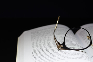 Reading glasses on open book and a dark background