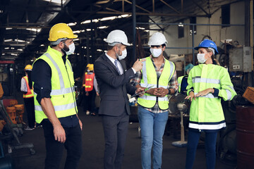 Leader or manager using tablet and meeting with engineer and technician while line walk in factory workplace, team wear face mask whine working at maintenance machine shop 