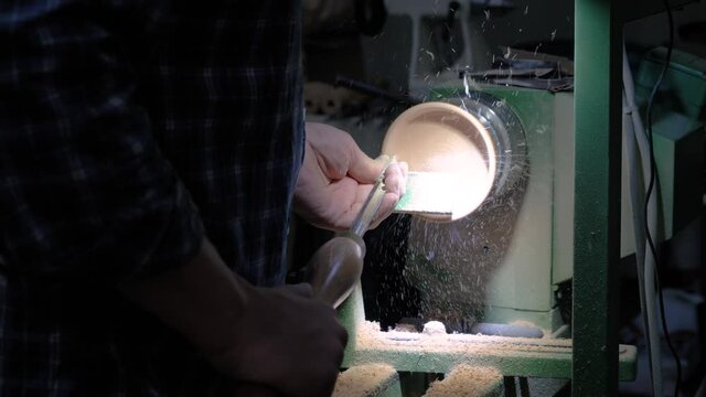 Carpentry, craftsmanship, design, manufacturing concept. Close up view - professional man carpenter using skew chisel for shaping piece of wood on wood turning lathe at workshop - slow motion