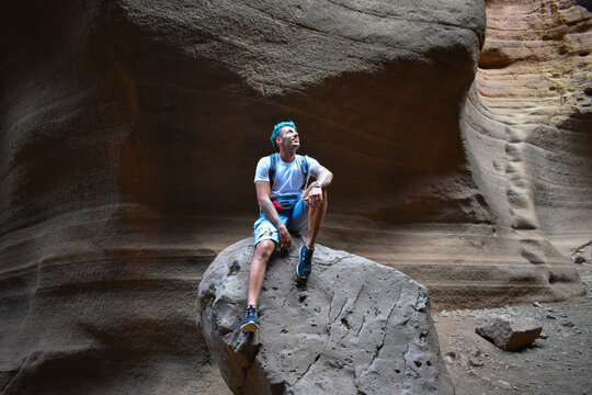 Young man sitting on some smooth and colorful volcanic stones, Tobas de Colores, Barranco de las Vacas.