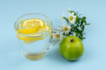 Glass cup with water and lemon slices, green apple and chamomile