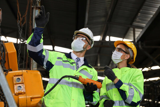 Manager or supervisor wear face mask talking or training with engineering team or worker about crane or machine control and operate in manufacturing plant or factory, Covid or virus protection