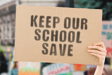 The phrase " Keep our school save " on a banner in men's hand with blurred background. Education. Studying. Security. Safety. Violation. Violation. Control. Surveillance. Protection