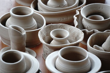 handmade unbacked crockery and pots on the table in the potter's studio. clay before firing in a...