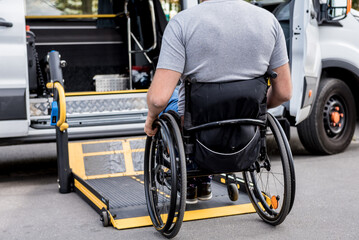 Obraz premium A man in a wheelchair on a lift of a vehicle for people with disabilities
