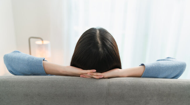 Back View Of Woman Resting Comfortably And Relaxing On A Sofa After Work At Home.