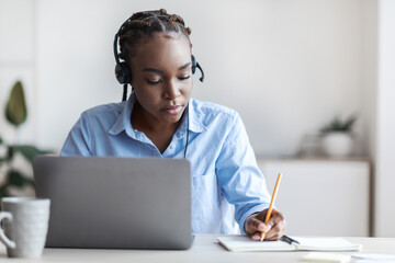 Online Training. Black female employee watching webinar on laptop and taking notes