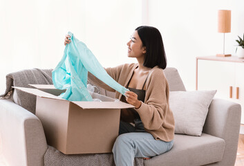 Happy asian buyer unpacking clothes after online shopping