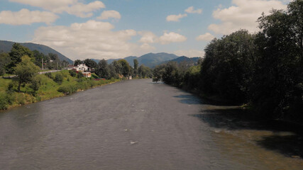 A full-flowing river flows past the trees. Forest river and house under the sky with clouds.