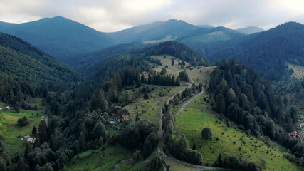 Forest mountains meadows and lonely houses. Green meadows and trees near the mountains against a gloomy sky.