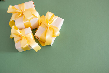 Christmas festive composition. Three gift boxes tied with a gold bow on a pastel green background. Flat lay, top view. Copy space for text.