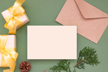Christmas festive composition. Blank sheet of paper, eco-paper mailing envelope and gifts on a pastel green background. Flat lay, top view. Copy space for text.