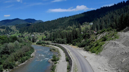 Clear fresh river beside a thin asphalt road. Mountain village is near the river.