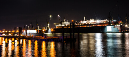 Fototapeta na wymiar Scenic widescreen night shot of large container vessel under repair in the dock on the Elbe river in Hamburg, Germany