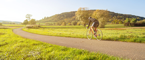 Panorama shot of cyclist on a racing bike in scenic rural autumn landscape during beautiful...