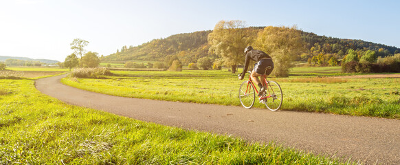 Panorama shot of cyclist on a racing bike in scenic rural autumn landscape during beautiful afternoon light