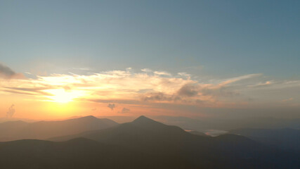 Rising sun over misty mountains. The peak of the mountain against the backdrop of a little cloudy foggy sky.