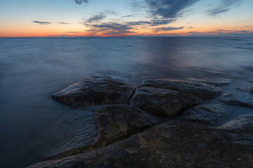 Twilight sunset over rocky shore of Baltic sea. Almost clear sky and orange strap along the horison. Estonia.