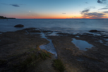 Fototapeta na wymiar Twilight sunset over rocky shore of Baltic sea. Almost clear sky and orange strap along the horison. Estonia.